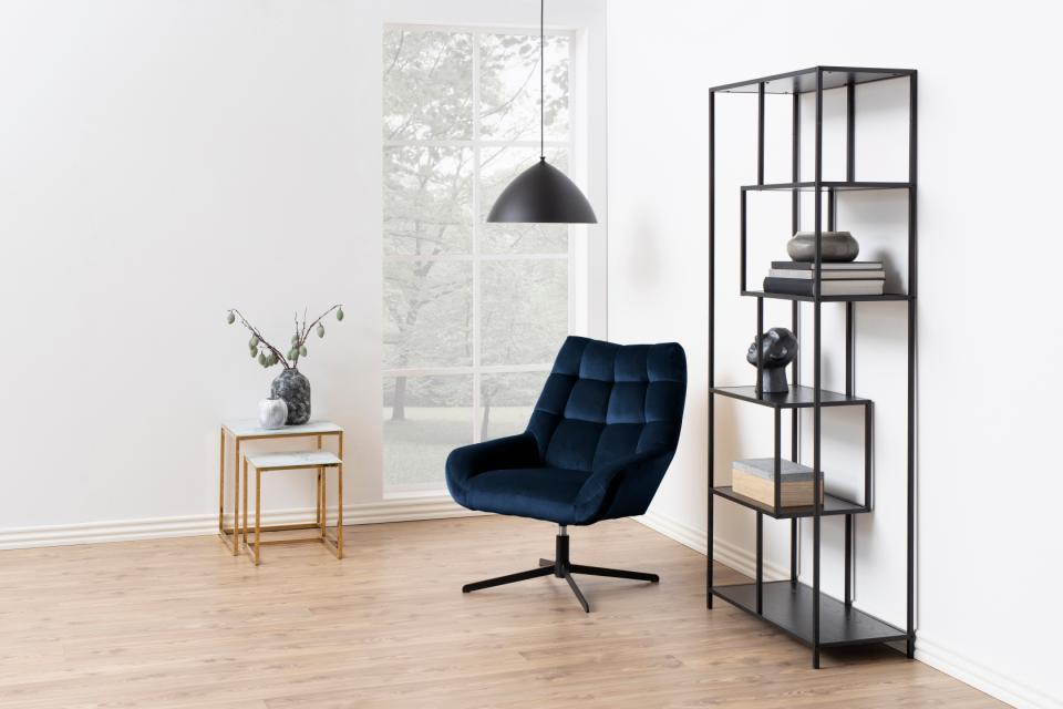 Modern interior with a blue armchair, black shelving unit, and gold side table.