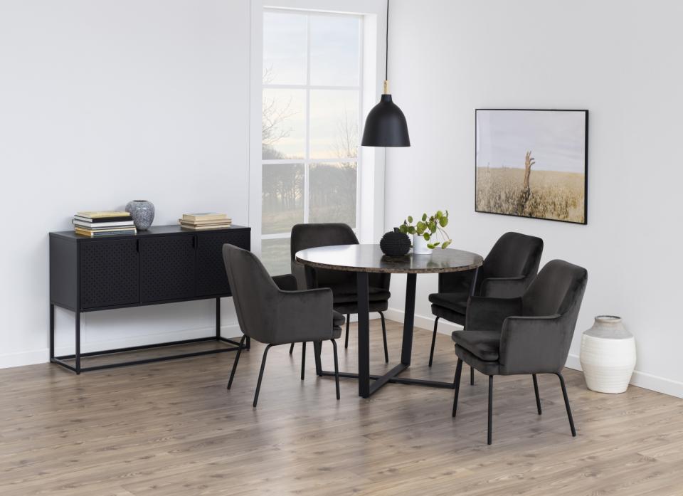A modern dining room set featuring a round dark wood table with a black metal base, surrounded by four dark gray upholstered chairs. A matching black sideboard cabinet stands against the white wall on the left, and a black pendant light hangs above the table.