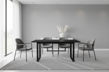 A modern dining room setup featuring a black rectangular table surrounded by four gray upholstered chairs with black metal frames, set on a light gray patterned rug against a minimalist gray wall.