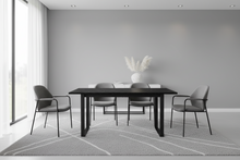 Load image into Gallery viewer, A modern dining room setup featuring a black rectangular table surrounded by four gray upholstered chairs with black metal frames, set on a light gray patterned rug against a minimalist gray wall.

