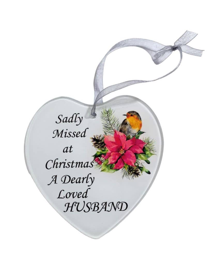 A white heart-shaped glass hanging decoration with a poinsettia flower and a robin. The text on the decoration reads 'Sadly missed at Christmas a dearly loved Husband'.