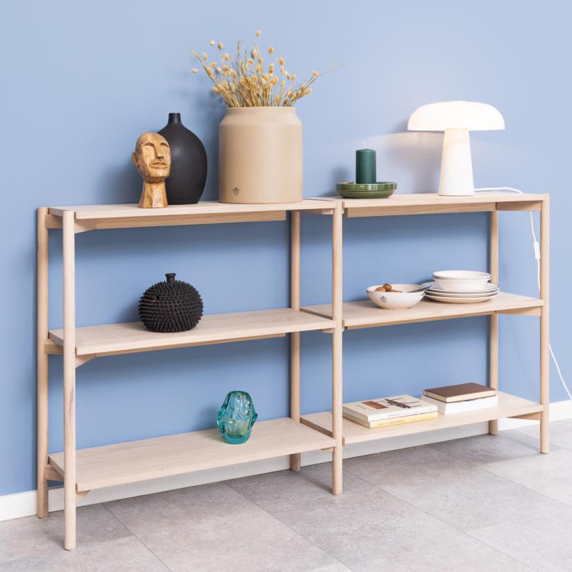 A light natural wood shelving unit with four tiers and open side supports, styled with home decor items against a blue wall.