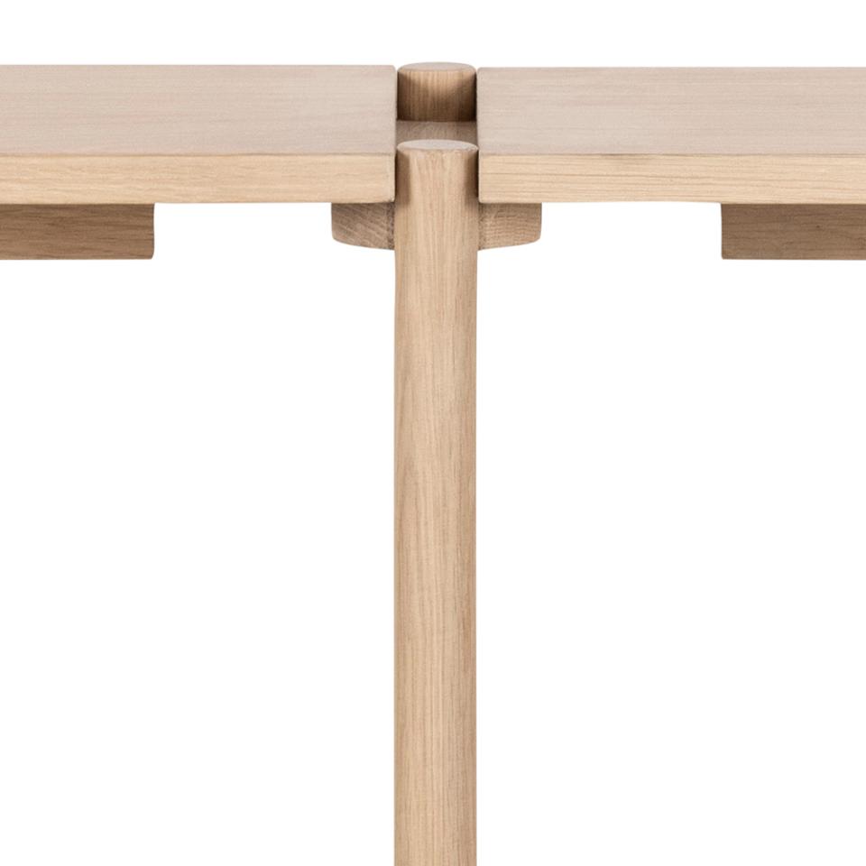 Close-up of a light natural wood table showing the joinery connection between the tabletop and the central pedestal leg, isolated on a white background.