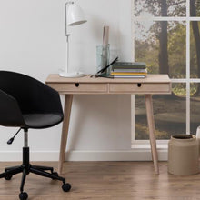 Load image into Gallery viewer, A light natural wood writing desk with two drawers and tapered legs, styled in a home office setting with a black office chair, white desk lamp, and books.

