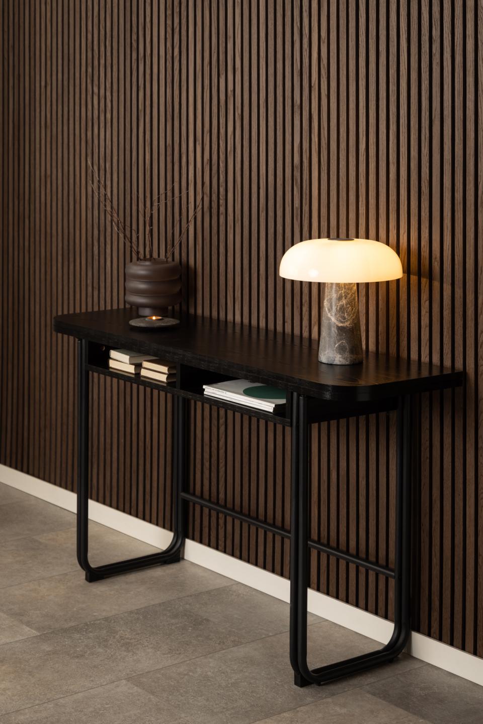 Modern black console table with a lamp and books against a striped wall.
