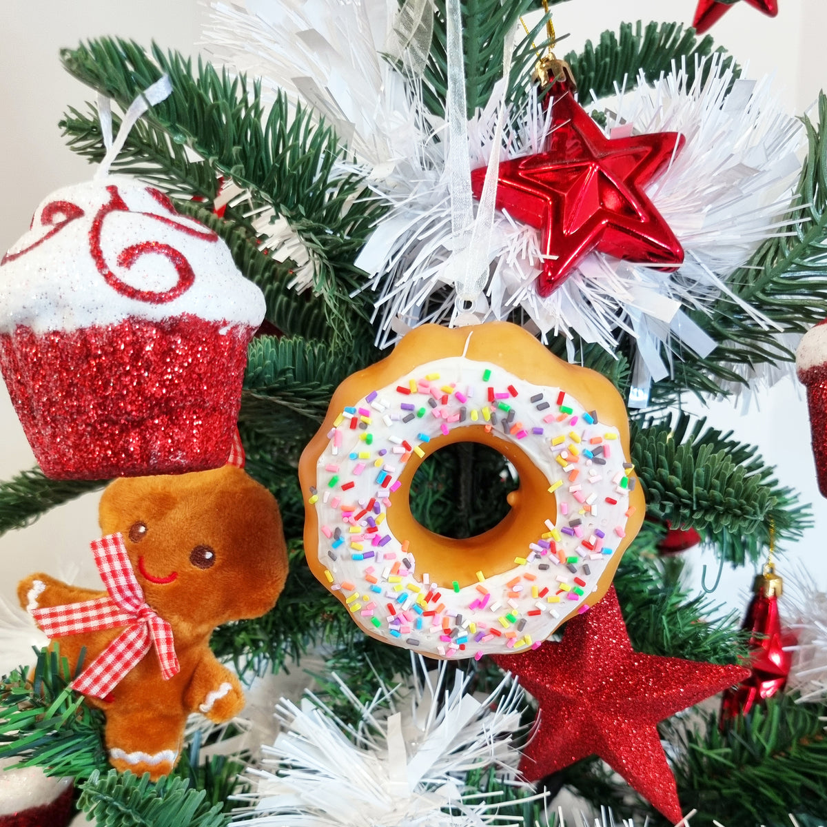 a plastic doughnut hanging on a Christmas tree with a gingerbread man, white tinsel and red stars