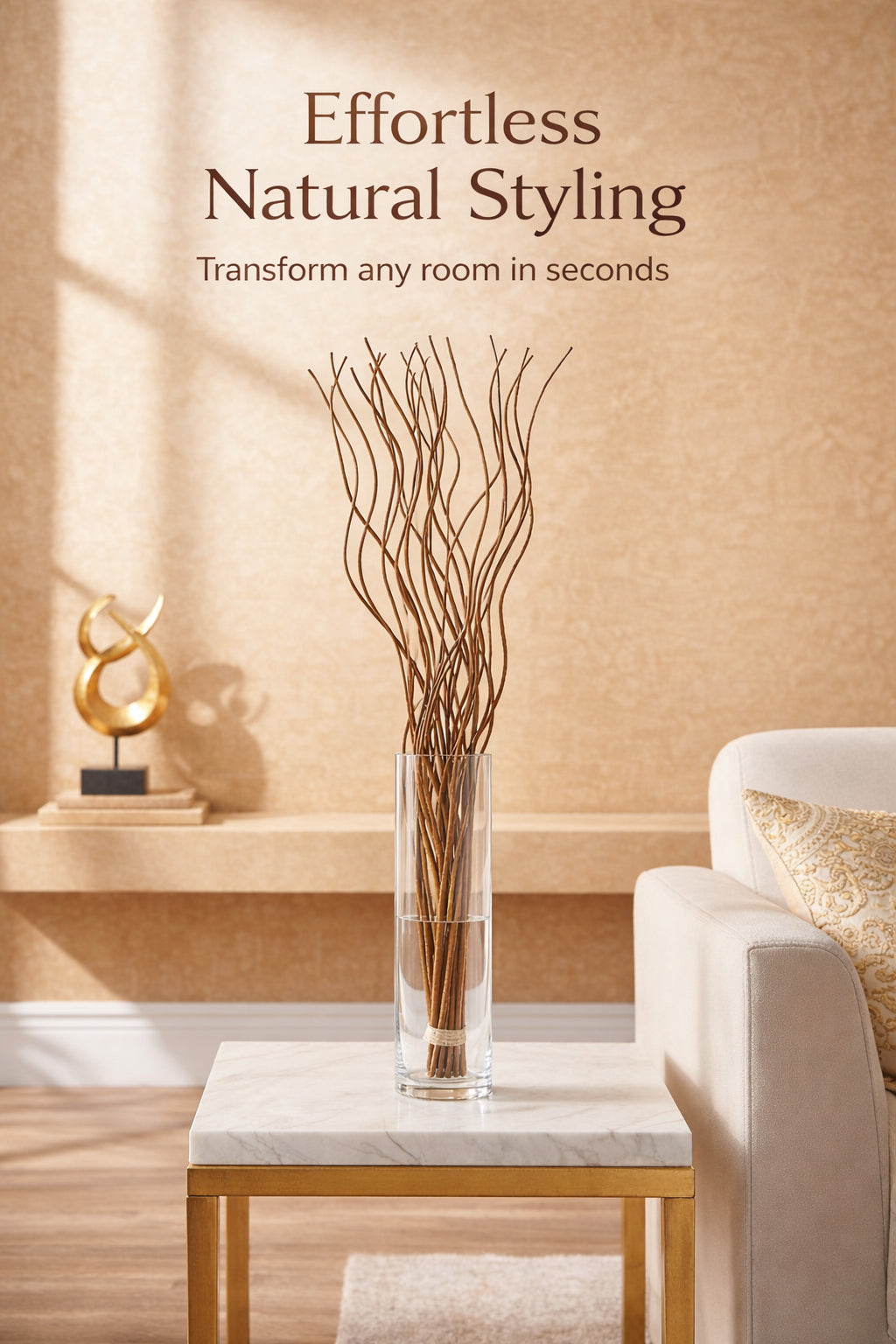 A clear cylindrical glass vase filled with dried brown branches, displayed on a marble-top side table in a styled living room. A cream sofa with a patterned pillow is visible on the right, and the wall above reads 'Effortless Natural Styling' with smaller text 'Transform any room in seconds'.