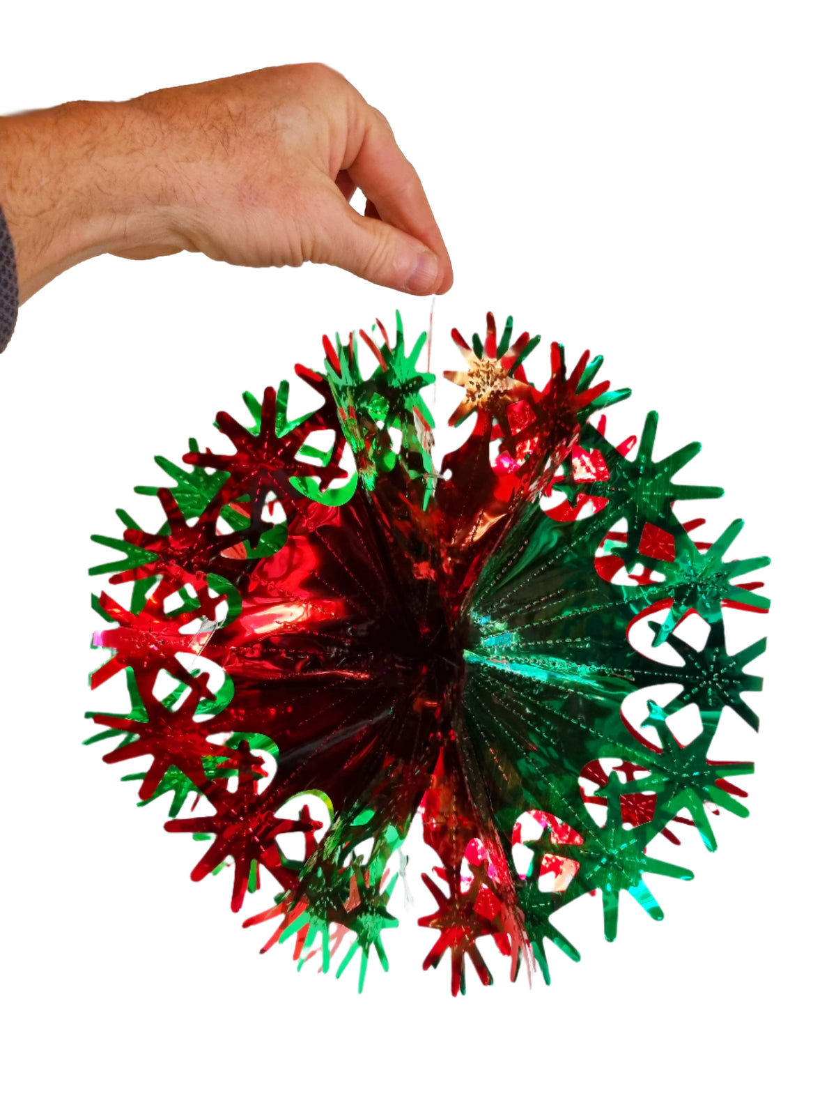 A hand holding a round, metallic Christmas ornament with a red and green starburst pattern and a small gold star at the center, isolated on a white background.