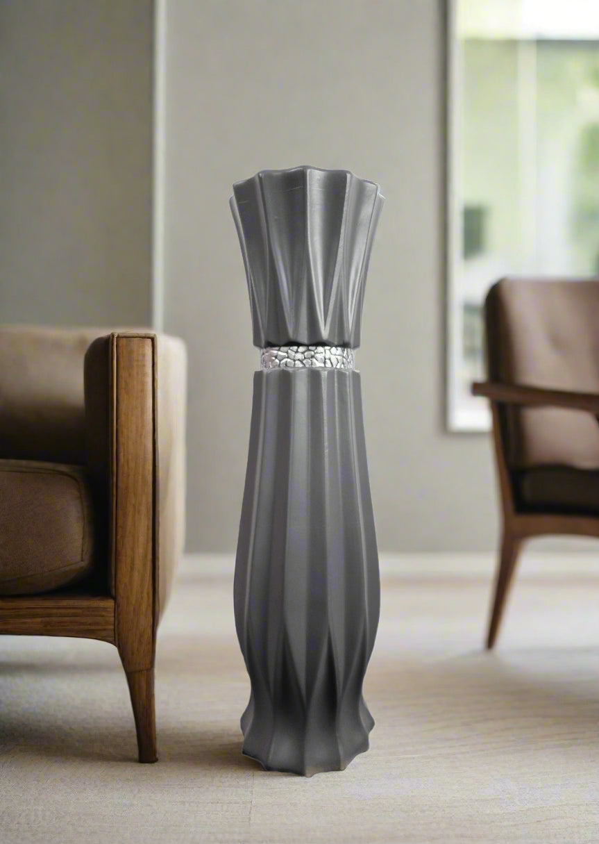 A modern gray sculptural vase with a fluted, pleated design and a textured metallic band at the waist, displayed in a minimalist living room setting.