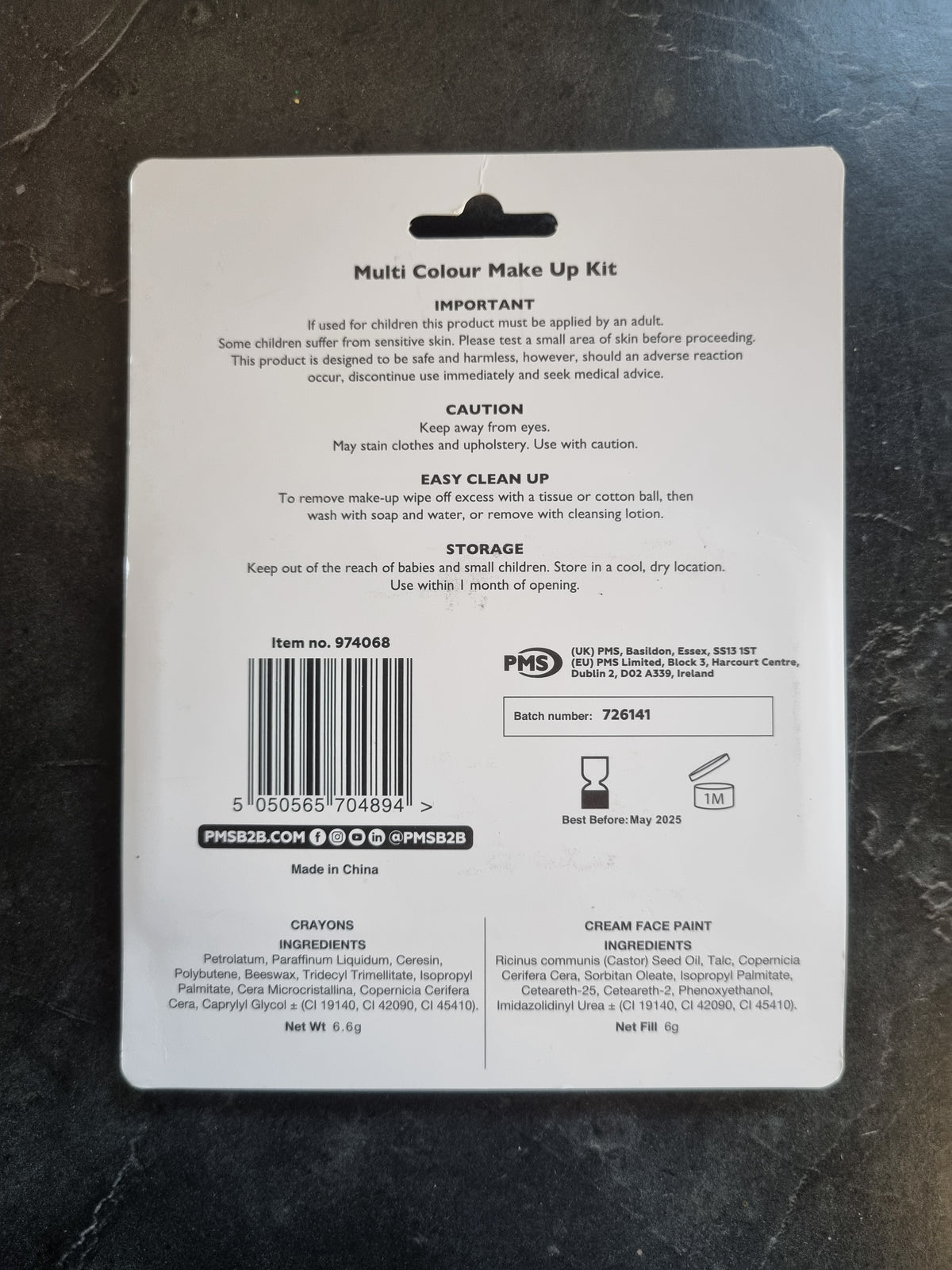 The back of a PHS Multi Colour Make Up Kit box, showing product information, barcode, and ingredients, placed on a dark marble surface.