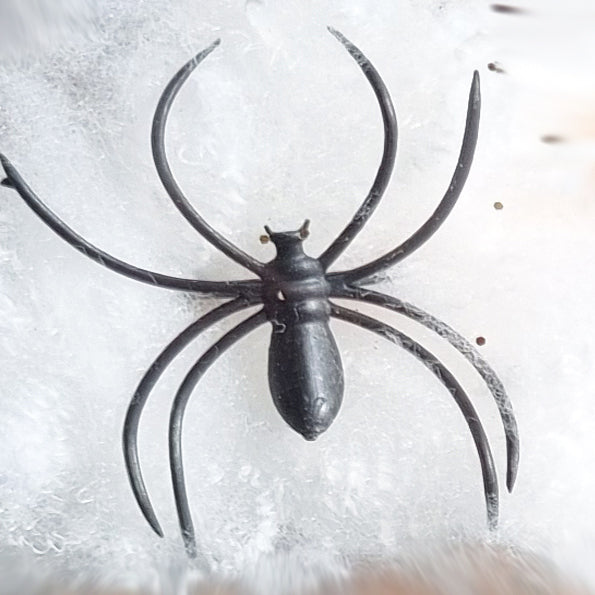 A black plastic spider-shaped hair claw clip or hair pin shown from above on a white textured background.