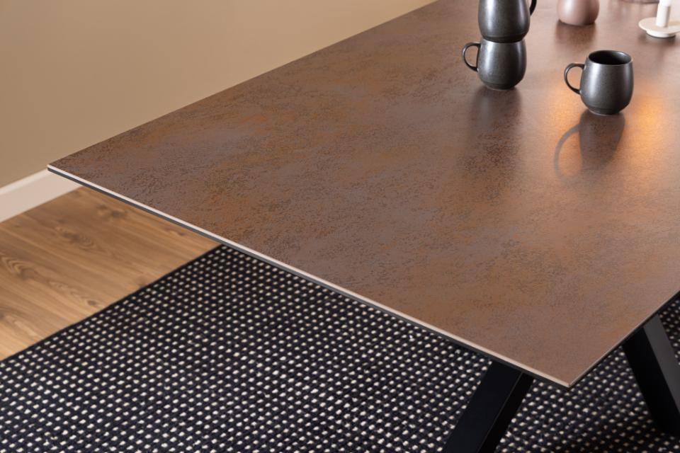 Brown ceramic table on a wooden floor with a black and white patterned rug.