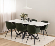 Load image into Gallery viewer, A modern dining room setup featuring a rectangular white marble-top table surrounded by six dark green upholstered chairs with black legs, set on a cream rug with a vase of flowers and a pendant light overhead.
