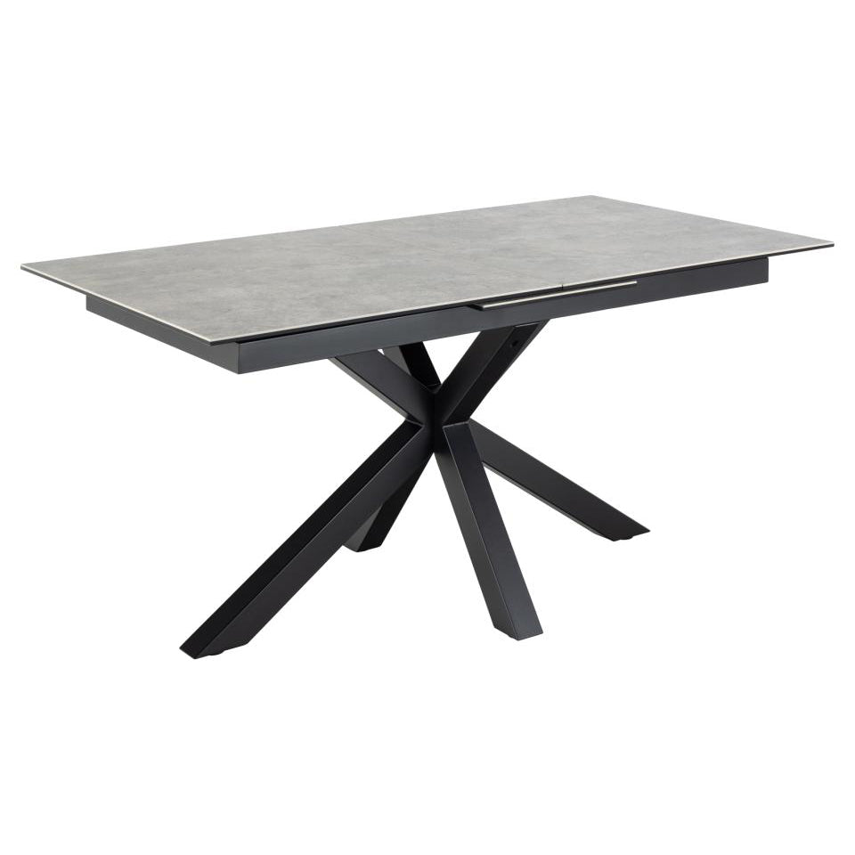 A modern extendable grey dining table with a ceramic top and a black metal cross base with the extension closed.
