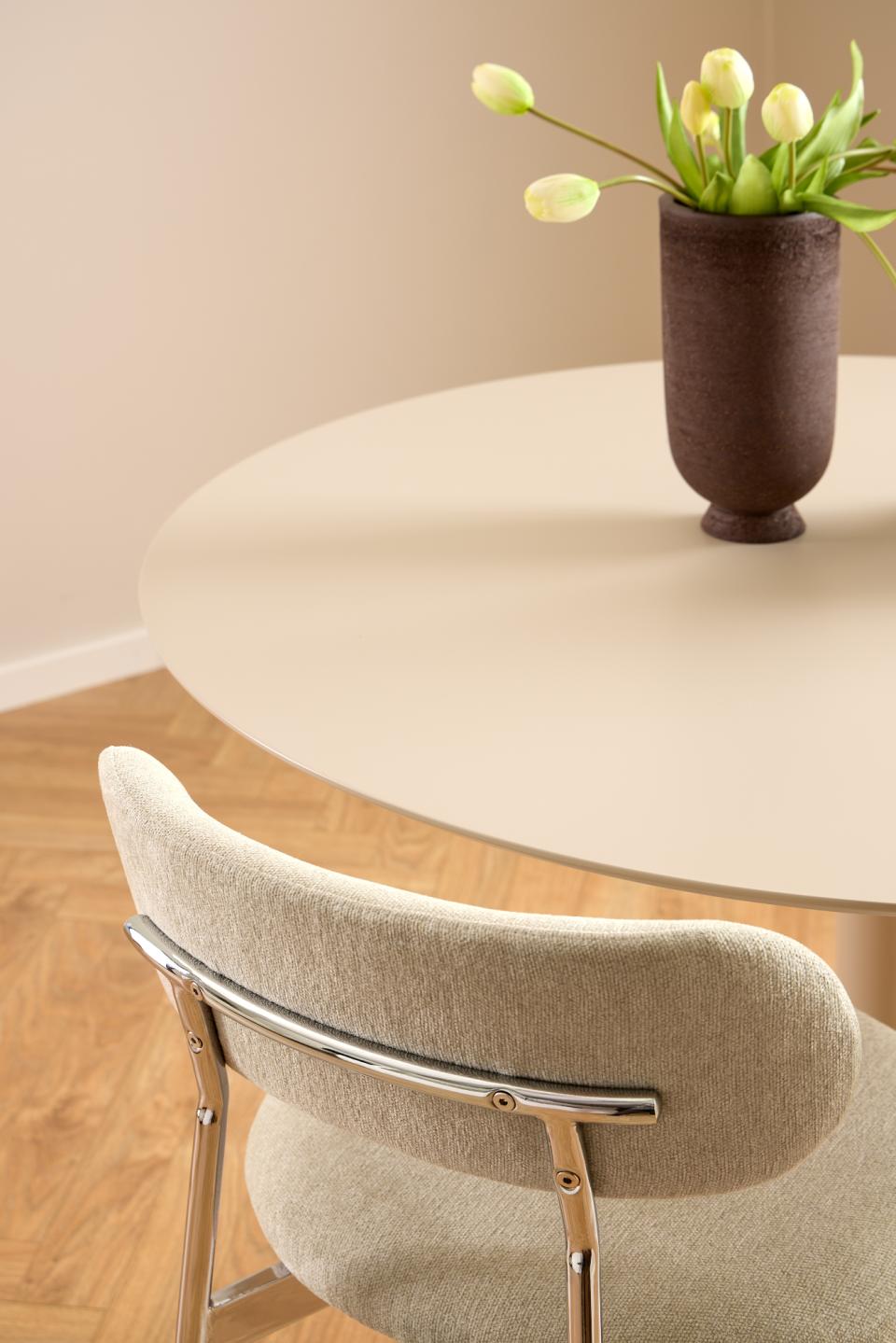 Round table with a vase of tulips and a chair in a room.