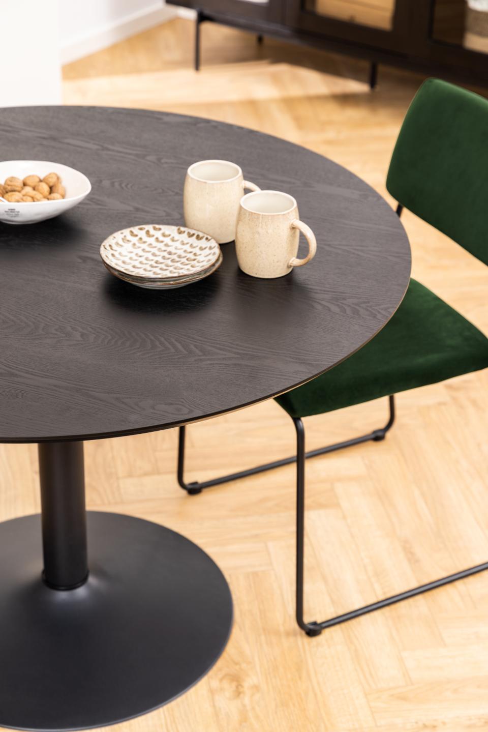Round black table with mugs and a bowl on a wooden floor