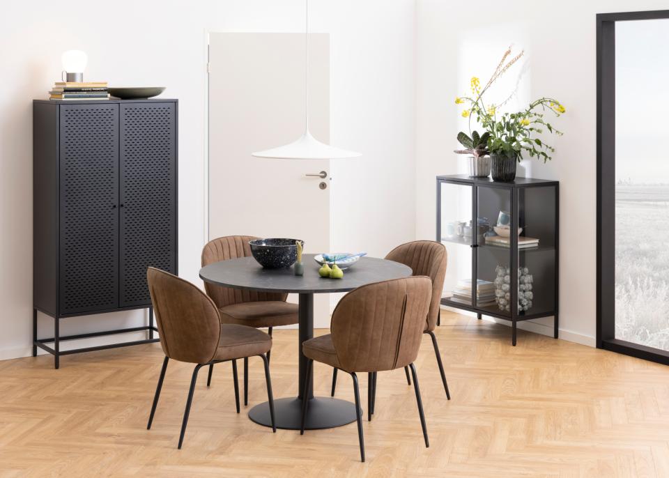 A modern dining set featuring a round black table and four brown upholstered chairs, styled in a bright, contemporary dining room with light wood floors and minimalist decor.