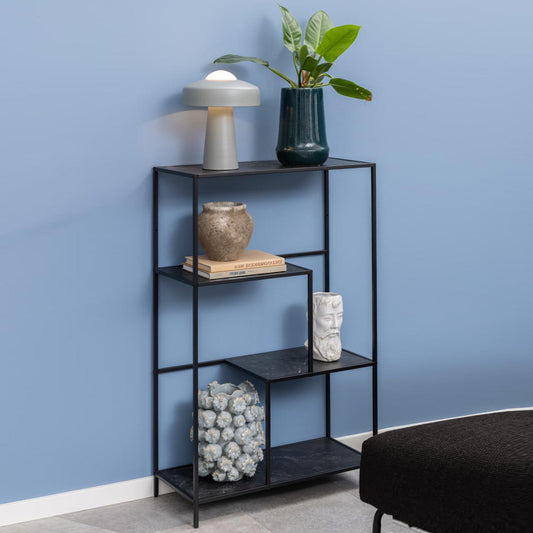 A black metal frame bookcase with three shelves, featuring asymmetrical detailing. The shelves have various decorative items and plants on them, placed against a blue wall.