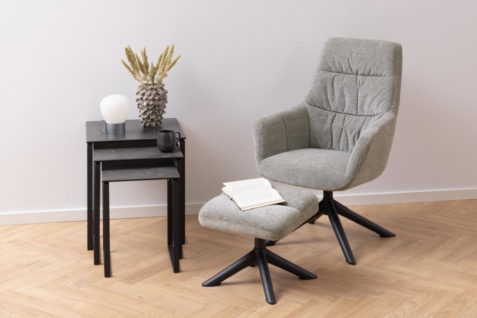 Gray armchair with ottoman and side table against a white wall