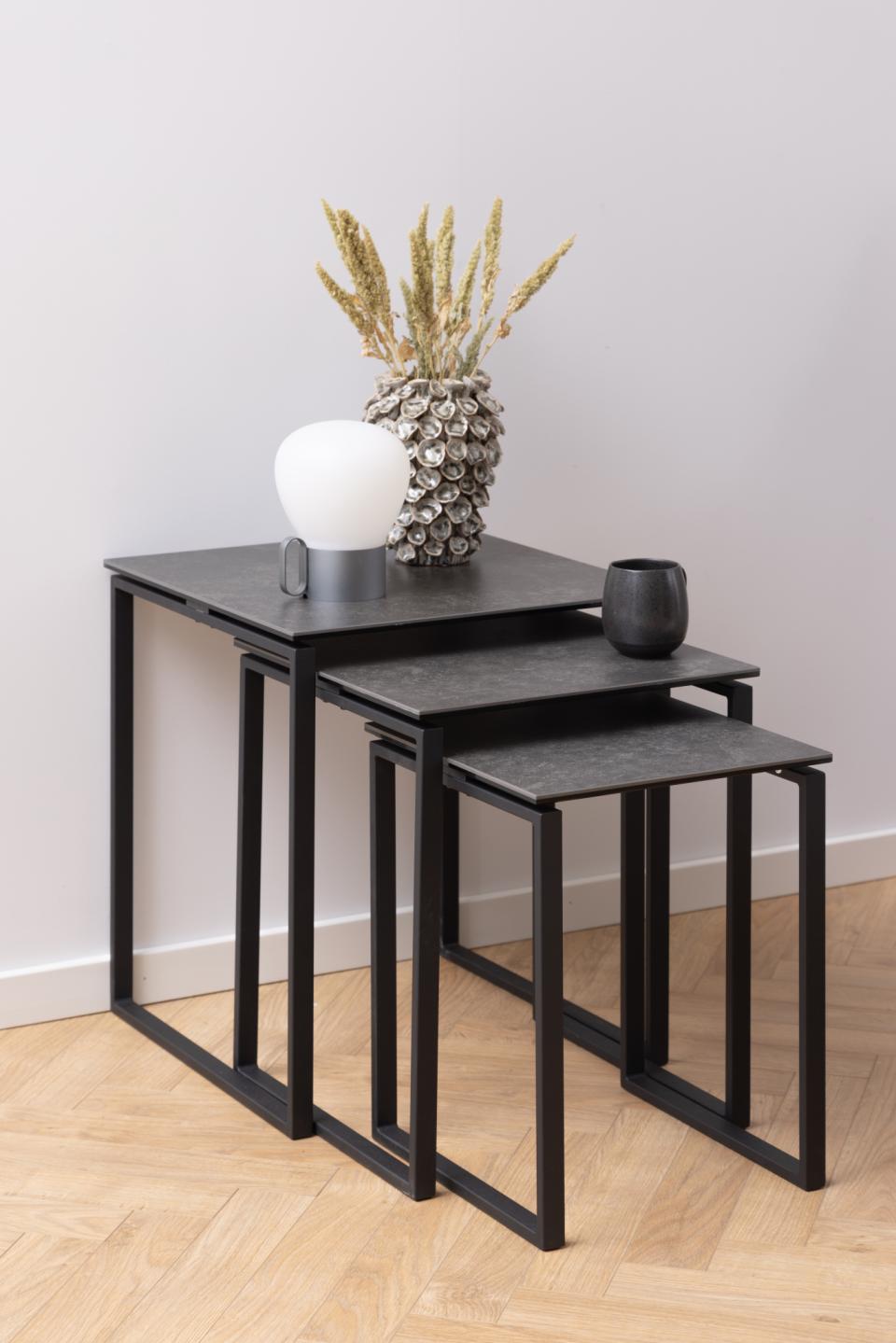 Set of three black nesting tables with decorative items on a light wood floor.