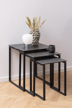 Load image into Gallery viewer, Set of three black nesting tables with decorative items on a light wood floor.
