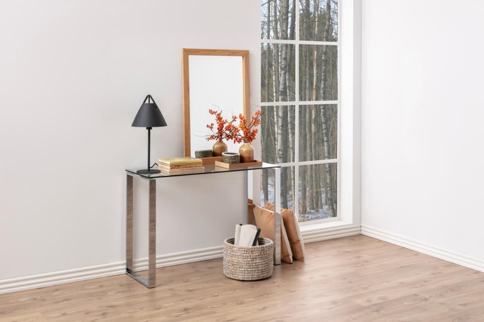 Console table with mirror, lamp, and decorative items in a room with large windows.