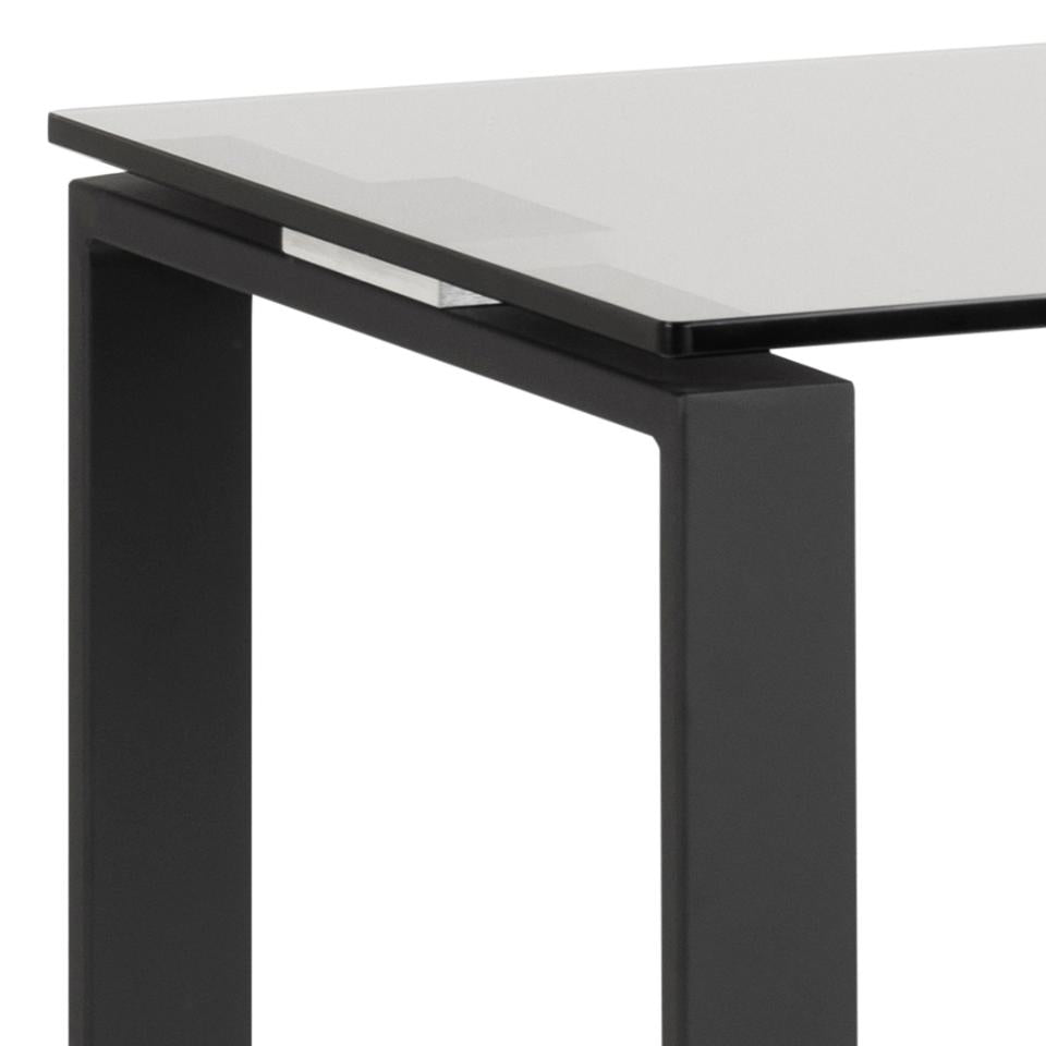 Close-up of a modern table corner showing a clear glass tabletop and a matte black metal frame leg on a white background.