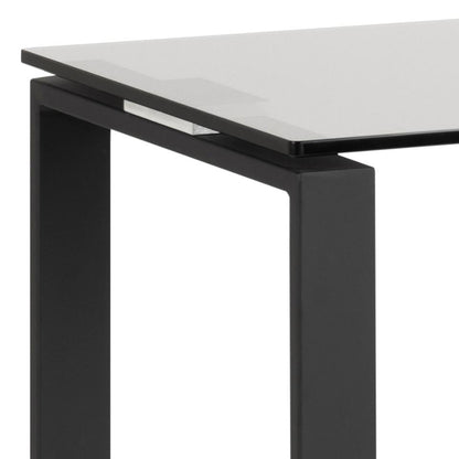 Close-up of a modern table corner showing a clear glass tabletop and a matte black metal frame leg on a white background.