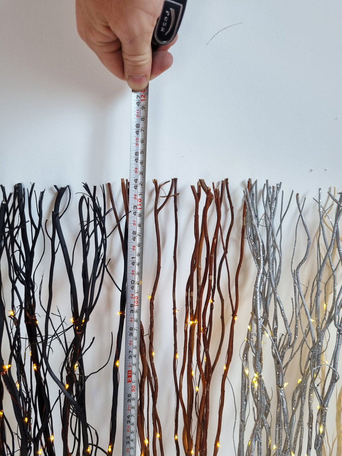 a hand with a tape measure above the led light up willow twigs measuring the height