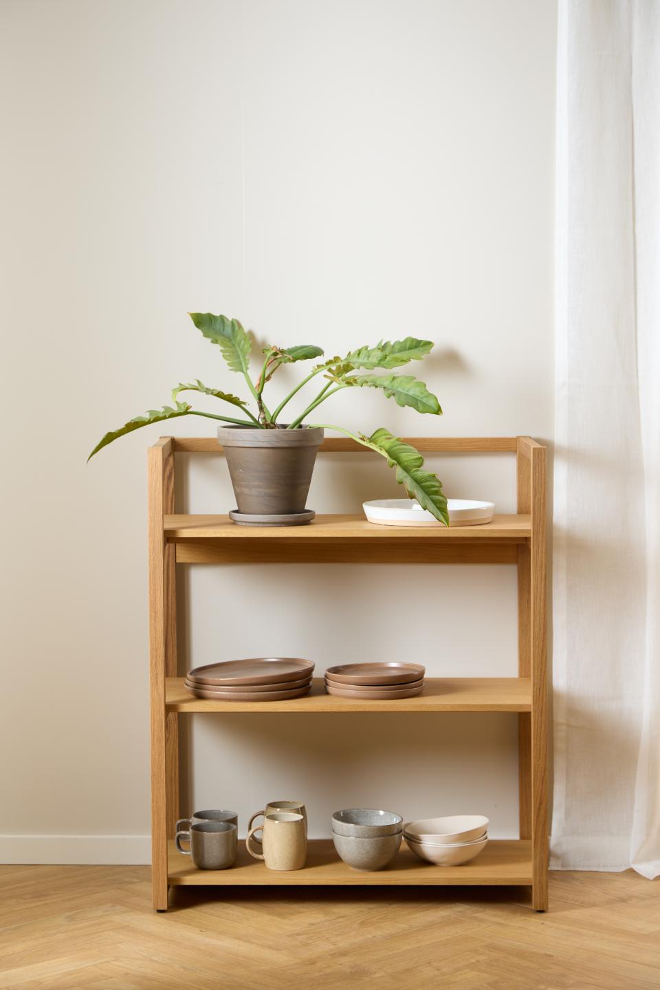Wooden shelf with decorative items including a plant, bowls, and mugs against a plain wall.