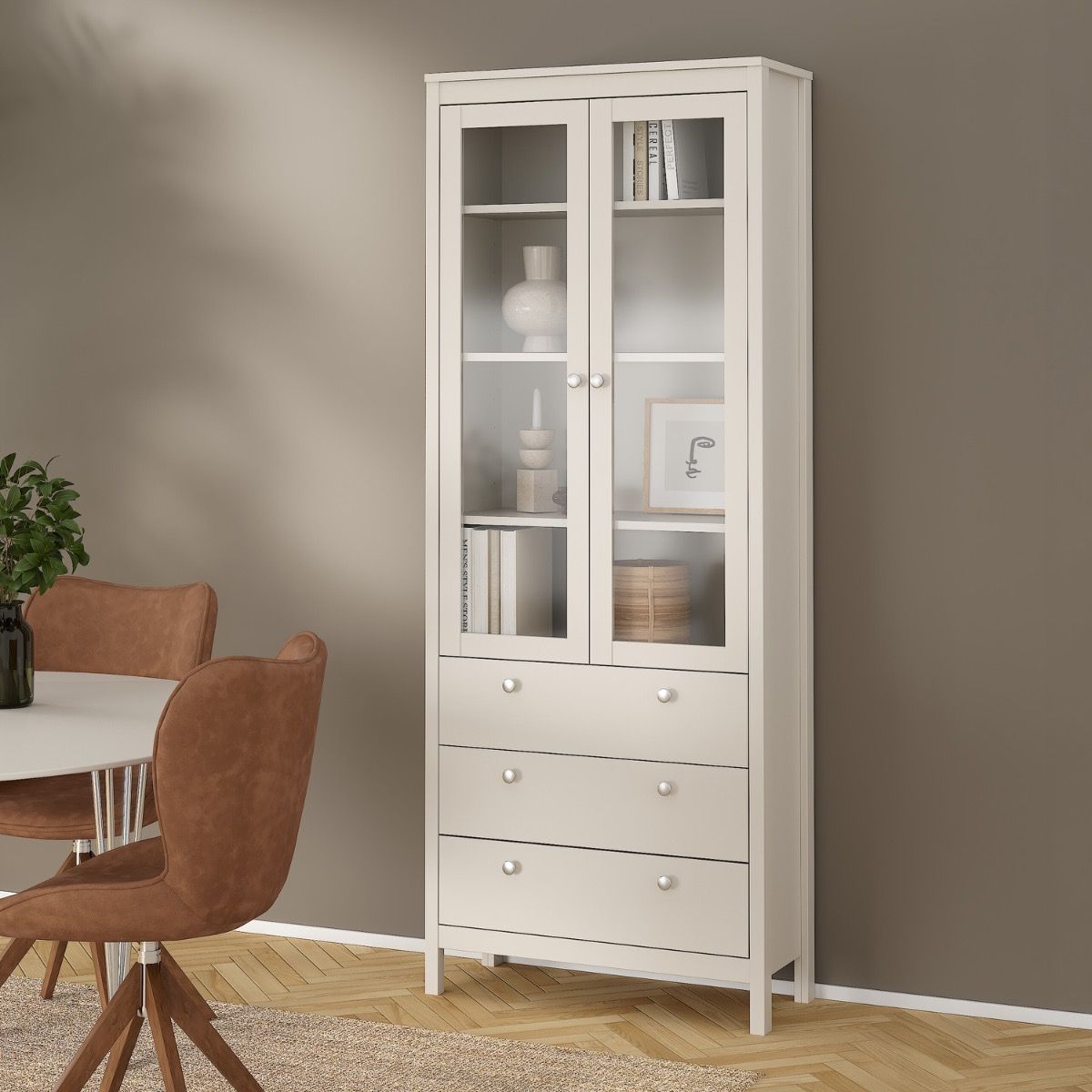 A Madrid cashmere glass display cabinet with two doors, three drawers and three shelves in a modern home with a brown wall, wood flooring, a rug and table and chairs