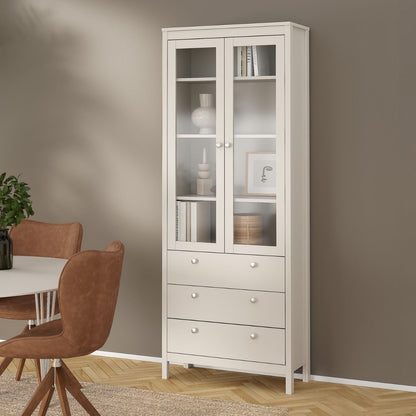 A Madrid cashmere glass display cabinet with two doors, three drawers and three shelves in a modern home with a brown wall, wood flooring, a rug and table and chairs