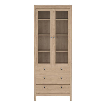 Front view of a brown light oak Madrid cabinet with two glass doors, three drawers and three shelves on a white background