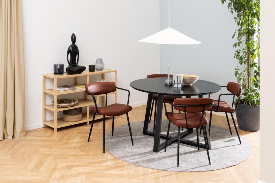 A modern dining set featuring a round black table and four matching chairs with brown leather upholstery and black metal frames, arranged on a round gray rug in a bright room.