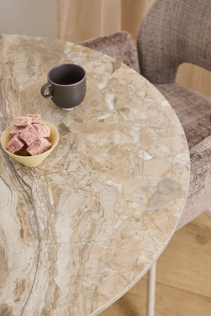 Round marble table with a cup and bowl of cookies on a wooden floor.