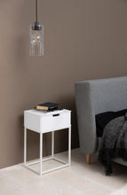 Load image into Gallery viewer, White nightstand with a lamp next to a gray upholstered chair against a brown wall.
