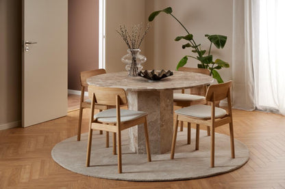 Dining room with a round marble table and wooden chairs on a wooden floor.