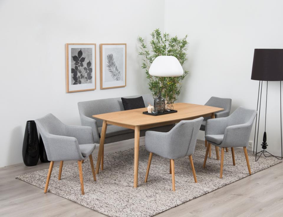 A modern dining set featuring a rectangular light oak wood table and six matching gray upholstered armchairs with light wood legs, arranged on a textured gray rug in a bright, minimalist dining room.