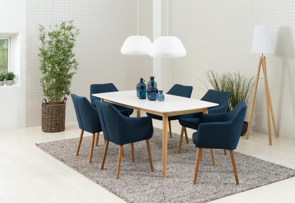 Dining room with a white table and blue chairs on a gray rug, surrounded by plants and lamps.