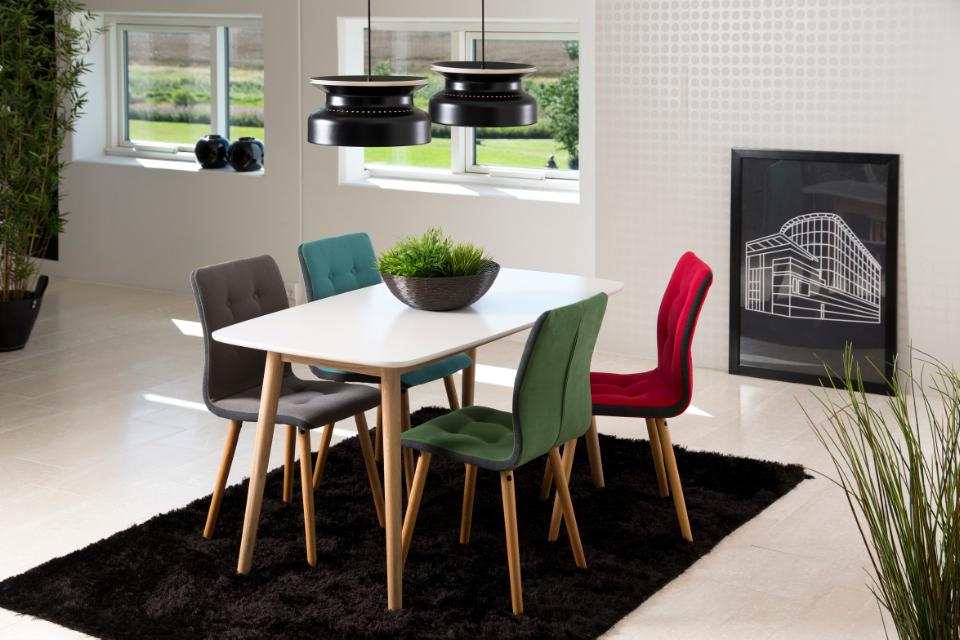 Modern dining area with a white table and colorful chairs on a black rug.