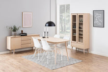 Load image into Gallery viewer, A light natural wood dining room furniture set in a bright, modern room. The set includes a sideboard, a tall glass-front cabinet, a rectangular dining table, four white chairs with wire legs, and a black dome pendant light, arranged on a gray patterned rug over light wood floors.
