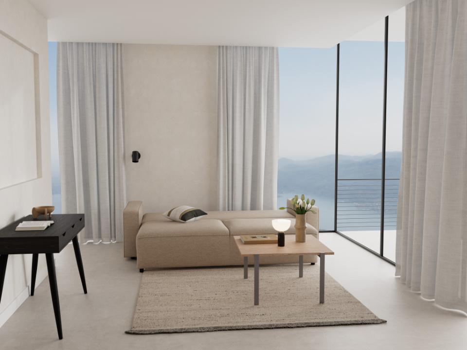 A modern beige sectional sofa in a minimalist coastal living room with a wooden coffee table, textured rug, and large floor-to-ceiling windows overlooking the sea.