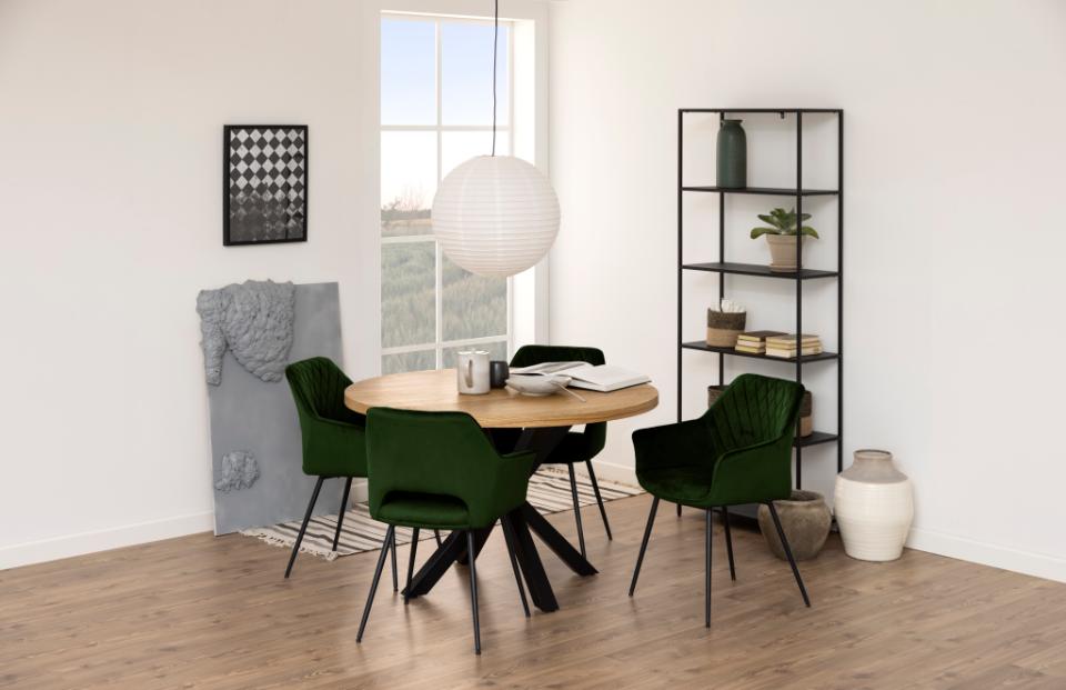 Modern dining room with round wooden table and green chairs, large window, and bookshelf.