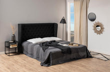 Load image into Gallery viewer, A modern bedroom scene featuring a bed with a tall, black tufted headboard, dressed in dark gray and black striped bedding with white pillows. The room has light wood floors, beige curtains, and minimalist decor including a black side table, floor lamp, and wall mirrors.
