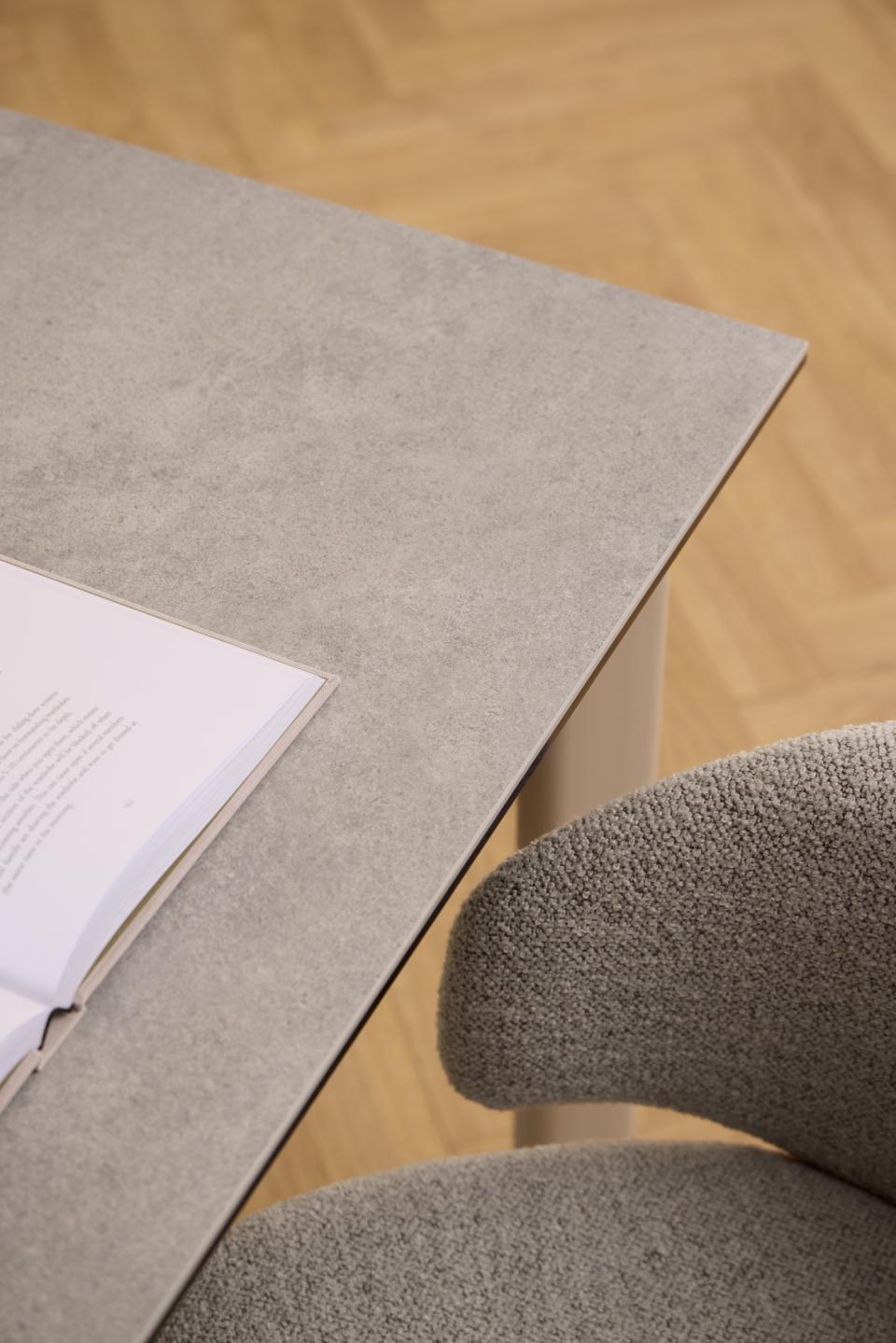 Close-up of a gray upholstered chair beside a matching gray table with an open book on top, set against a light wood herringbone floor.