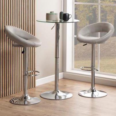 A taupe faux leather bar stool with a cushioned seat and back rest, chrome base and foot rest, positioned in a room with a glass table.