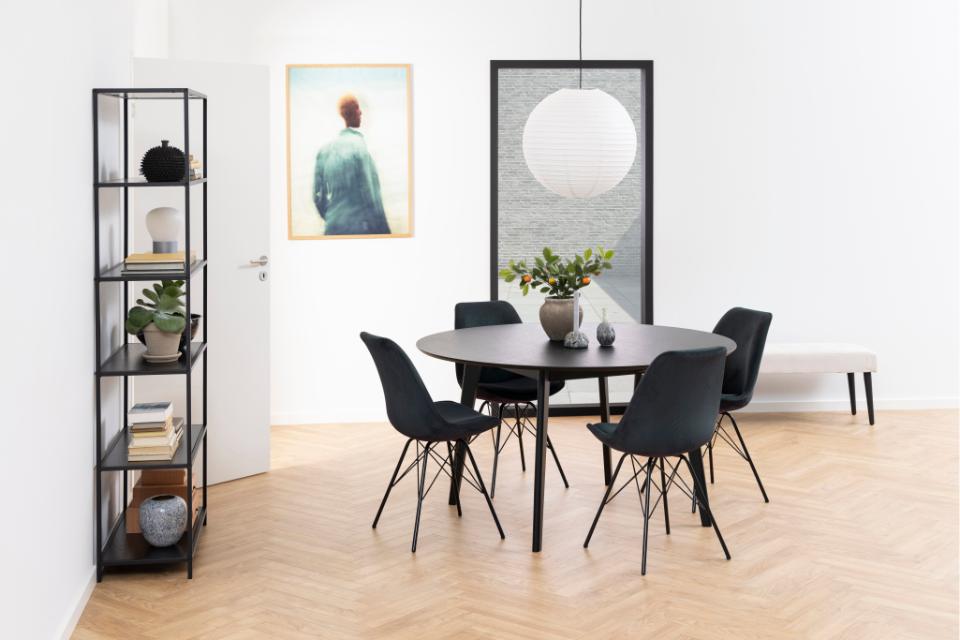 Modern dining room with round table and chairs, bookshelf, and artwork on the wall.