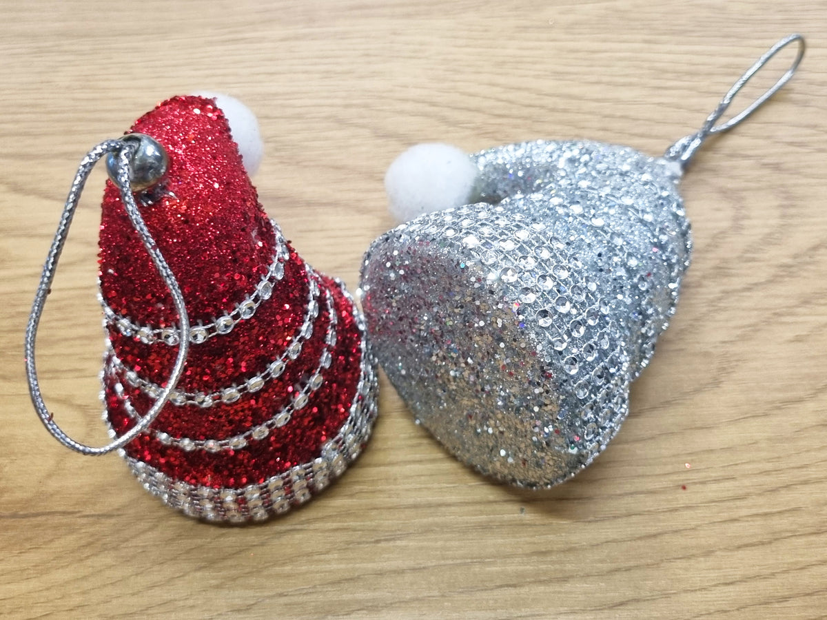 2 santa hats in red and silver resting on a wooden surface