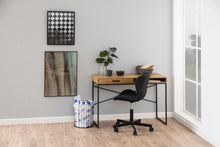 Load image into Gallery viewer, A modern home office setup featuring a wooden desk with a single drawer and black metal frame, paired with a black swivel office chair. The desk is styled with a small potted plant, a mug, and a basket, set against a light gray wall with framed art and a window on the right.
