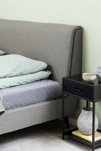 Load image into Gallery viewer, Gray upholstered bed with green bedding and a black nightstand with decorative items.
